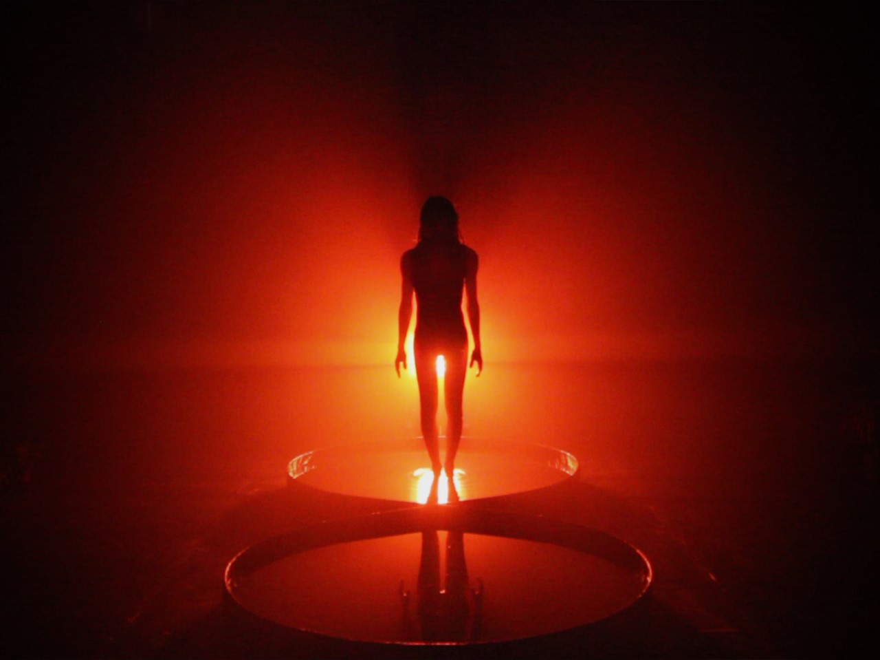 A performance consiste numa experiência imersiva e etérea, num ecossistema habitado pela artista e pelo público onde duas paisagens corporificadas intersetadas desdobram-se, mapeando a sua identidade e circunscrevendo a sua transição. A visão cenográfica da peça transporta a audiência para a simplicidade absoluta de um trabalho sobre o corpo, a mente e a alma. Propondo a observação atenta de atos como o de despertar, respirar, levantar, secar, transitar e revelar que simultaneamente contêm ousadia e vulnerabilidade. O espelho de água em forma de infinito, a emanação sonora, o vestido celestial e a presença dos quatro elementos naturais contribuem para uma atmosfera de outro mundo alcançada pelo uso do tempo e meticulosa escultura do espaço. 7 ≈ 8 é o culminar de uma profunda introspeção e da coragem de desconstruir e reconstruir a sua própria história, partilhando-a.