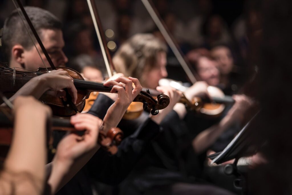 Fotografia de músicos a tocar violino durante uma performance de música clássica, capturando a concentração e a habilidade dos instrumentistas. A imagem é ideal para promover concertos de música clássica em Lisboa, destacando a dedicação e a elegância da orquestra