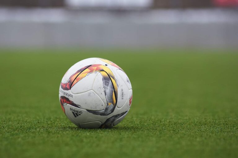 Fotografia de uma bola de futebol em um campo de relva verde, pronta para o jogo. A imagem é ideal para destacar o calendário de jogos de futebol na TV portuguesa, ajudando os fãs a saber onde assistir às partidas ao vivo. Perfeita para o tema 'Onde dá a Bola - Hoje'.