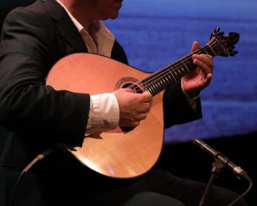 Fotografia de um músico a tocar guitarra portuguesa durante uma atuação de fado, destacando a elegância e a tradição desta música. A imagem é perfeita para promover os melhores locais em Lisboa para ouvir fado ao vivo, capturando a essência cultural e emocional do fado.
